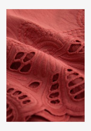 Embroidered fabric in a rich rust color, featuring intricate floral patterns and cut-out details, with a soft, textured surface.