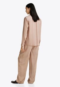 Beżowa, w paski koszula z długim rękawem i luźne spodnie, wykonane z miękkiego materiału. Subtelny detal w postaci guzików z przodu, z podwiniętymi mankietami.