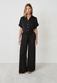 Zwarte twee-delige outfit bestaande uit een kortärmige, button-up blouse met kraag en een broek met wijde pijpen, elastische taille en trekkoord.