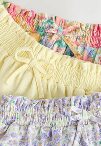 Három elasztikus derékpántos szoknya masnival, virágmintákkal rózsaszín, sárga és lila árnyalatokban, fehér háttéren fekve.