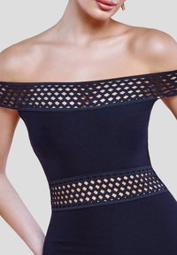 Off-shoulder navy kjole med ribbet stof, der har et mønstret blonderbånd ved halsudskæringen og taljen, som fremhæver udskæringsdetaljer.