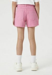 Shorts en denim rose avec ourlet effiloché, design à cinq poches et détail de couture à l'arrière, associés à des baskets blanches et des chaussettes.