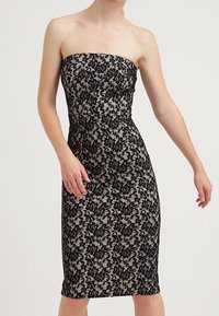 Utan axelband spetsklänning med ett svart blommönster över en nude-basis. Figursydd design, knälång, med en slät textur.