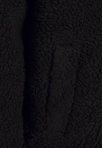 Tejido de forro polar negro con una superficie suave y texturizada. Presenta un patrón elevado y esponjoso junto con un área lisa y plana. Sin herrajes o adornos visibles.