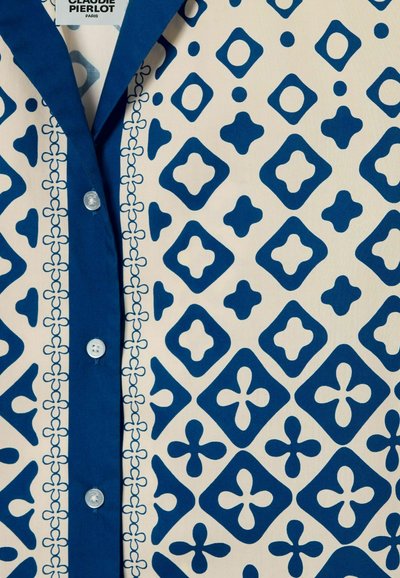 Camicia a righe blu e bianche con motivi geometrici, chiusura a bottoni e colletto e placket blu uniforme. Tessuto di cotone testurizzato.