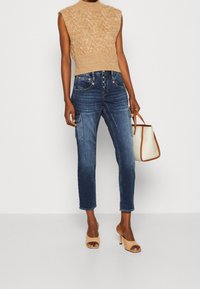 Stickad beige ärmlös topp med texturmönster, bärs med blå högmidjade jeans med cargofickor, ihop med beige öppna klackar.