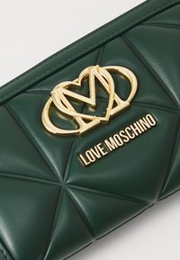 Zeleno kviltano faux usnjeno denarnico z zlatim srčkom in logotipom "LOVE MOSCHINO". Oprijemljive šive in gladko teksturo.