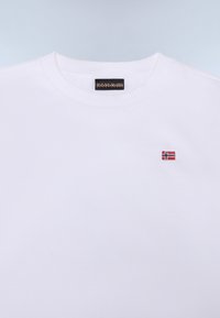 Hvit bomulls T-skjorte med et lite brodert norsk flagg-logo på venstre bryst. Klassisk rund hals og ribbet krage-design.