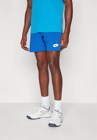 Μπλε αθλητικό σορτς από ελαφρύ ύφασμα, με λευκό λογότυπο στην αριστερή πλευρά και ελαστική μέση. Συνδυάζεται με λευκά αθλητικά παπούτσια.