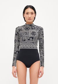 Maillot de bain à manches longues avec un design à motifs noirs et blancs, featuring des motifs géométriques et floraux. Col montant et silhouette ajustée.