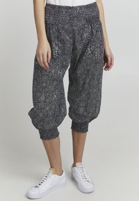 Svarta och vita mönstrade harembyxor med elastisk midja och muddar, tillverkade av lättviktsmaterial. Bärs med vita sneakers.