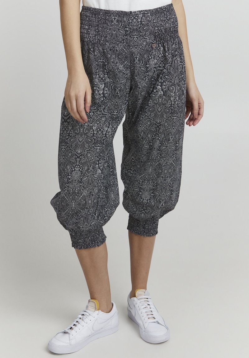 Svarta och vita mönstrade harembyxor med elastisk midja och muddar, tillverkade av lättviktsmaterial. Bärs med vita sneakers.