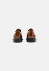 Un paio di scarpe da dress in pelle marrone lucida mostrate dal retro su uno sfondo bianco, con dettagli brogue e suole nere.