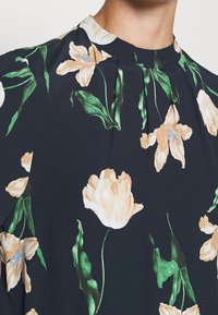Květinová blůza s vysokým výstřihem, na tmavě námořnickém pozadí se světlými a modrými květinami, se zelenými listy a jemnými sklady.