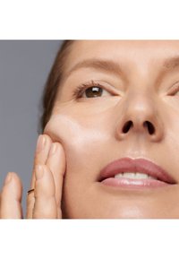 Gros plan sur un visage appliquant un produit de soin crémeux. La peau semble lisse et hydratée, avec un éclat naturel. Teint clair.