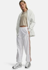 Grijze rits-hoodie, beige cropped top, witte sweatpants met roze zijstrepen en zilveren sportschoenen. Eenvoudig en sportief ontwerp.