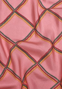 Tissu rose avec un motif géométrique de losanges festonnés en rouge, vert, jaune et orange, présentant une texture lisse et légèrement brillante.