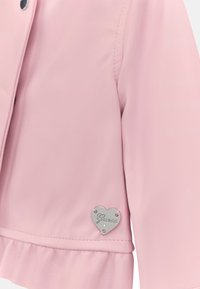 Różowa kurtka z sztucznej skóry z falbaną u dołu. Posiada srebrny detal w kształcie serca na dole z wygrawerowaną nazwą marki.