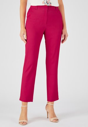 Pantaloni fucsia con design a gamba dritta, caratterizzati da una parte frontale piatta, passanti per la cintura e tessuto morbido e liscio. Indossati con sandali con tacco beige.