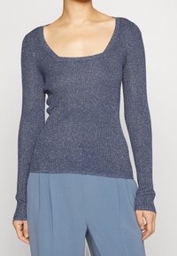 Haut à manches longues côtelé bleu marine avec un décolleté carré et des accents de fil métallique, associé à un pantalon bleu clair ajusté.