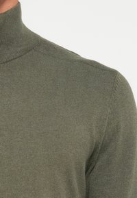 Olive green turtleneck sweater made of ribbed knit fabric. Fitted shape with subtle seams and a smooth texture. No visible patterns or accents.