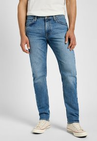 Ljusblå denimjeans med rak passform, femfickorsdesign och dragkedja. Matchat med off-white kanvas-sneakers.