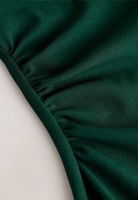 Close-up of dark green fabric with gathered elastic detail creating small folds along the edge.