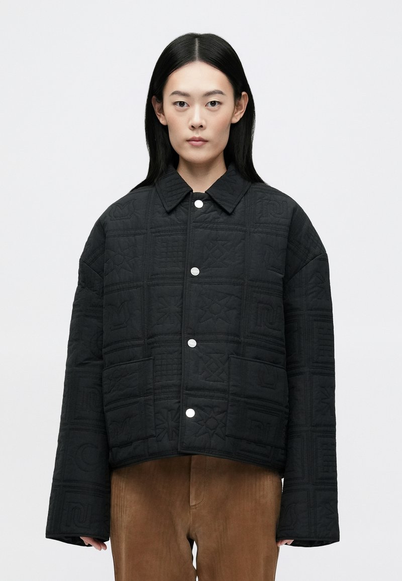 Mustmust mustriseljak, millel on kastikujuline lõige, tõstetud mustrid, nupud ja terav krae. Sile tekstuur ja madalad õlad.