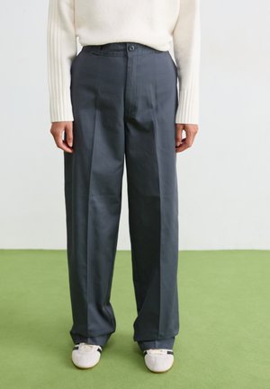 Dark gray trousers with a tailored fit, pleats, and a single button closure. Smooth texture and straight-leg design. White sneakers.