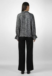 Bluse i leopardprint i lysegrå, med klokkeærmer og rund halsudskæring, parret med sorte vide bukser og høje ankelstøvler.