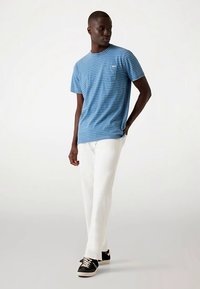 Kék csíkos rövid ujjú póló, kerek nyakkivágással és mellzsebbel, fehér nadrággal és fekete tornacipővel párosítva.