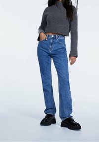 Suéter corto de punto acanalado gris con mangas largas, combinado con jeans rectos de cintura alta azul y zapatos negros de suela gruesa.