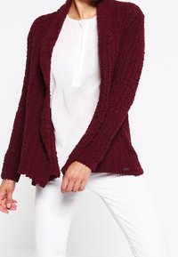 Bordeaux geklede cardigan met een open voorkant ontwerp, gemaakt van een zachte stof, met een losse pasvorm en lange mouwen. Witte shirt eronder.