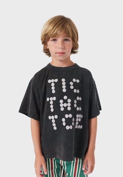 Zwarte t-shirt met korte mouwen en een ronde halslijn, met grote, witte, ronde letters die "TIC TAC TOE" spellen. Textuurcontrast van de stof.