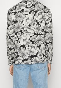 Bloemenprint lange mouwen shirt in zwart en wit met een verscheidenheid aan bloemenpatronen. Beschikt over een klassieke kraag en knopenmanchetten, gecombineerd met lichtblauwe jeans.