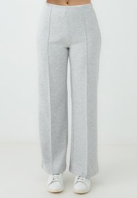 Helle graue weite Sweatpants aus weichem, meliertem Stoff mit vorderen Nähten und einem figurbetonten Bündchen, kombiniert mit weißen Sneakers.