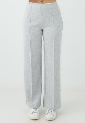 Helle graue weite Sweatpants aus weichem, meliertem Stoff mit vorderen Nähten und einem figurbetonten Bündchen, kombiniert mit weißen Sneakers.