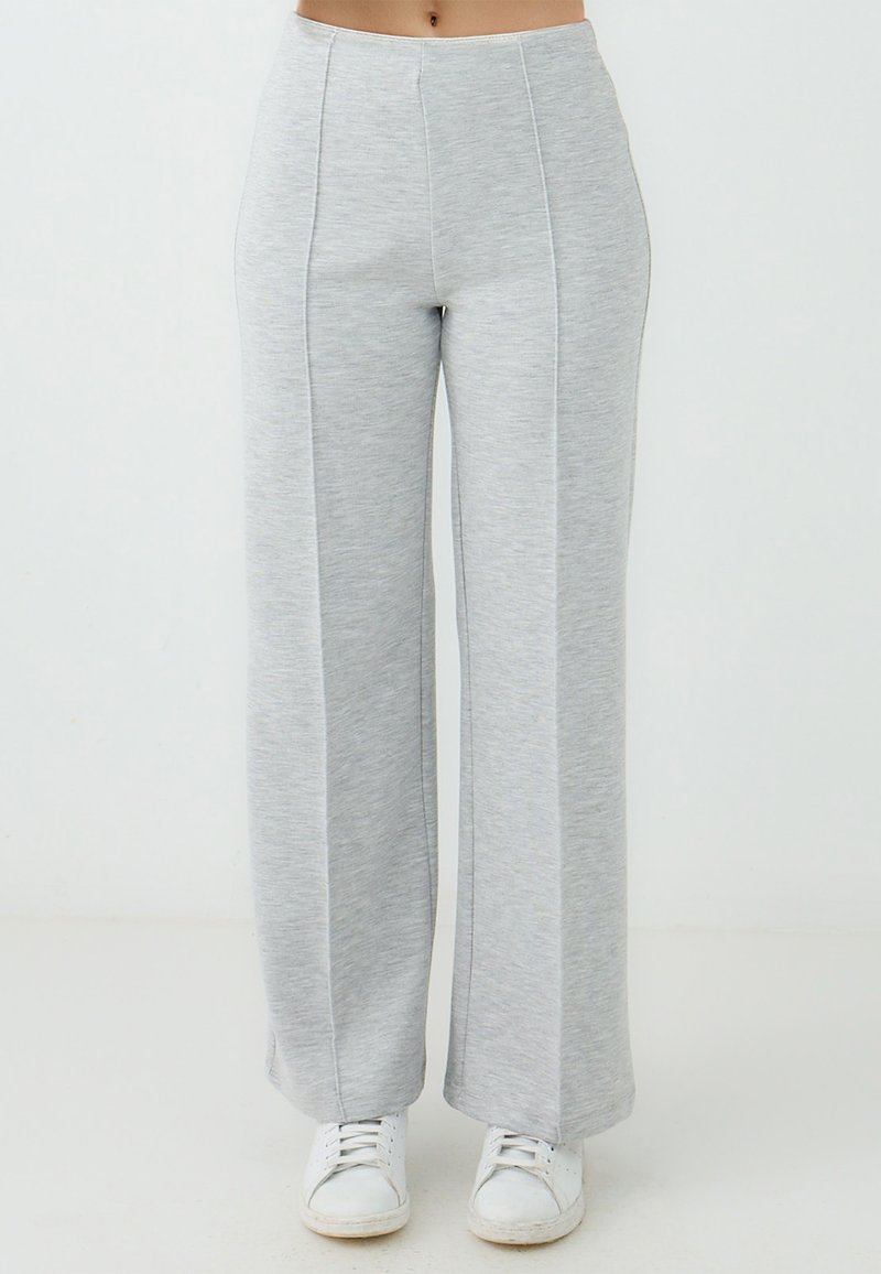 Helle graue weite Sweatpants aus weichem, meliertem Stoff mit vorderen Nähten und einem figurbetonten Bündchen, kombiniert mit weißen Sneakers.