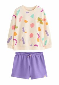 Ljusbeige sweatshirt med färgglada geometriska mönster och texten "Jag tror på mig själv," i kombination med lila shorts med dragsko. Mjuka material.