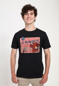 Černé tričko s vintage grafickým designem se usmívající krávou označenou „La Vache qui rit“. Design využívá červené a krémové barvy s texturovaným pozadím.
