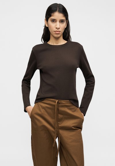 Καφέ μπλούζα με μακριά μανίκια και ριμπ ύφανση, συνδυασμένη με καφέ παντελόνι σε φαρδιά γραμμή, με πλαϊνές τσέπες και ελαστική μέση με κορδόνι.
