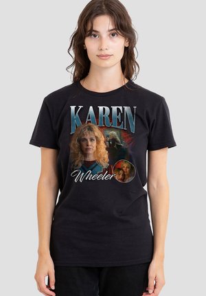 Young woman wearing black t-shirt with "Karen Wheeler" text and images of a blonde woman from a TV show or movie on a plain background.