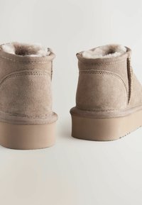 Brązowe zamszowe botki za kostkę z miękkim sztucznym futrem wewnątrz, zaokrąglony kształt i płaska gumowa podeszwa. Widoczne szwy na górnej części.