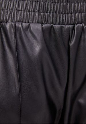 Pantalon en cuir noir avec une surface texturée, une taille froncée et une coupe décontractée, mettant en valeur la douceur et la fluidité.