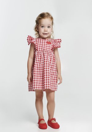 Robe en vichy rouge et blanc avec des manches à volants, taille froncée et broderie cerise. Associée à des ballerines rouges.