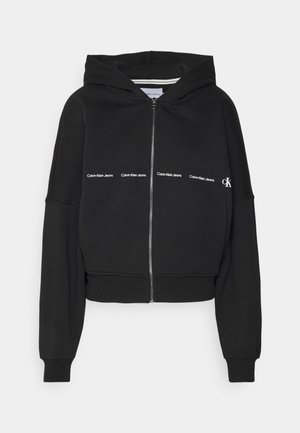 Sweat à capuche noir zippé avec capuche, manches longues, et texte blanc « Calvin Klein Jeans » ainsi que le logo « CK » sur la poitrine.