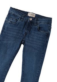 Jeans de mezclilla azul oscuro con un corte ajustado, diseño de cinco bolsillos y cierre de botón, con una etiqueta en la cinturilla.