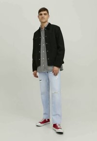 Μαύρο τζάκετ από τζιν πάνω από πουκάμισο με μαύρες και λευκές καρό ρίγες, συνδυασμένο με ανοιχτό μπλε σκισμένο τζιν και κόκκινα αθλητικά παπούτσια.