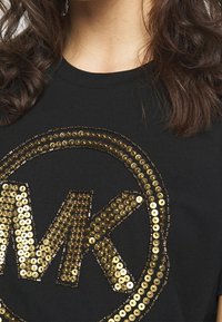 Svart bomull t-shirt med en cirkulär design i guld paljetter och en "MK"-logotyp i mitten, som framhäver blanke ytor.