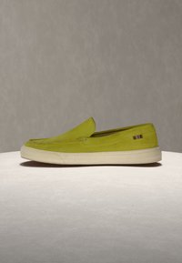 Πράσινο lime παπούτσι τύπου slip-on με λευκή λαστιχένια σόλα και μικρή λωρίδα υφασμάτινη λεπτομέρεια σε ουδέτερο φόντο.